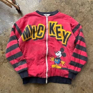 May include: A red zip-up jacket with the word "MICKEY" in yellow block letters across the chest. The jacket features black and gray striped sleeves and a cartoon image of Mickey Mouse. The jacket has a black collar and cuffs.