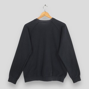 May include: A solid black long-sleeve sweatshirt featuring a crew neckline and raglan sleeves. The garment is displayed on a wooden hanger against a plain light gray background, showcasing a simple design with ribbed cuffs and a ribbed hemline.