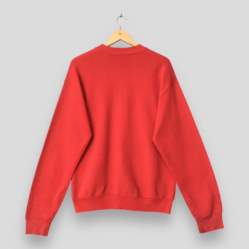 May include: A solid red sweatshirt with a crew neck and long sleeves. The sweatshirt is hanging on a wooden hanger against a light gray background. The fabric appears to be a soft, comfortable material.