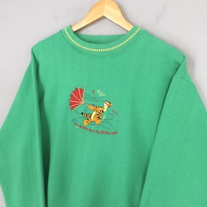 May include: Green sweatshirt featuring an embroidered image of Tigger from Winnie the Pooh holding an umbrella in the wind. The text "It's a Whiffletry day in The 100 Aker Wood" is below the image. The sweatshirt has a yellow and white striped collar.