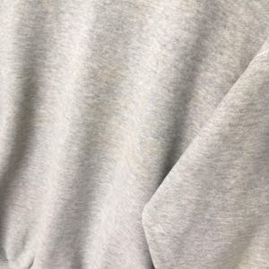 Puede incluir: Una sudadera de color gris claro jaspeado con una textura de tela suave y moteada. La prenda muestra un patr&oacute;n de tejido consistente con sutiles variaciones de tono en todo el material, creando un aspecto cl&aacute;sico y neutro en la superficie.