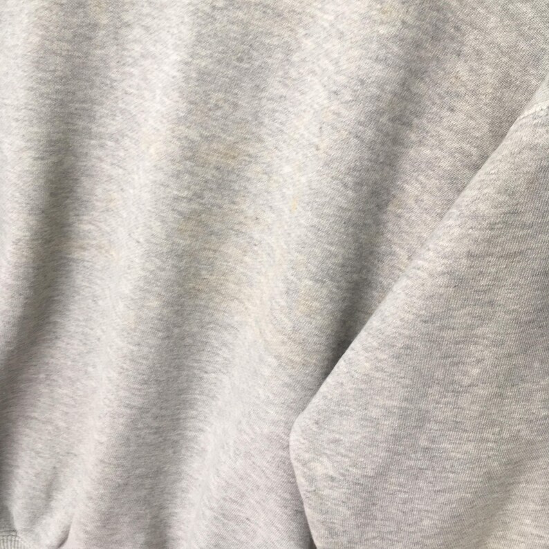 Puede incluir: Una sudadera de color gris claro jaspeado con una textura de tela suave y moteada. La prenda muestra un patr&oacute;n de tejido consistente con sutiles variaciones de tono en todo el material, creando un aspecto cl&aacute;sico y neutro en la superficie.