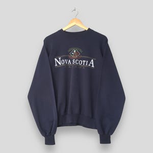 May include: Navy blue sweatshirt with the text "Nova Scotia Canada" in white and a crest design. The sweatshirt is hanging on a wooden hanger. The sleeves are long and the cuffs are ribbed.