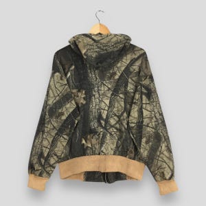 May include: A hooded camouflage jacket with a full zipper, displayed from the back. The jacket features a brown and tan color scheme with a forest pattern. The cuffs and hem are a solid tan color.
