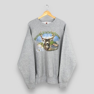 Puede incluir: Una sudadera gris con un gráfico que presenta un ciervo, peces y patos, con el texto "OUTDOOR HUNTING & FISHING" en verde. La sudadera tiene mangas largas y cuello redondo.