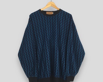 Puede incluir: Un suéter de manga larga con un patrón geométrico texturizado en azul oscuro y negro. La prenda tiene un cuello redondo negro sólido, puños negros y un dobladillo negro. Una etiqueta de marca rectangular marrón es visible en el cuello.
