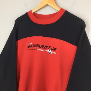 Puede incluir: Una sudadera vintage de cuello redondo en negro, rojo y blanco. La sudadera presenta el texto "Dale Earnhardt Jr." y el n&uacute;mero "8" en blanco. El logotipo de Budweiser tambi&eacute;n es visible. La sudadera est&aacute; colgada en una percha de madera.