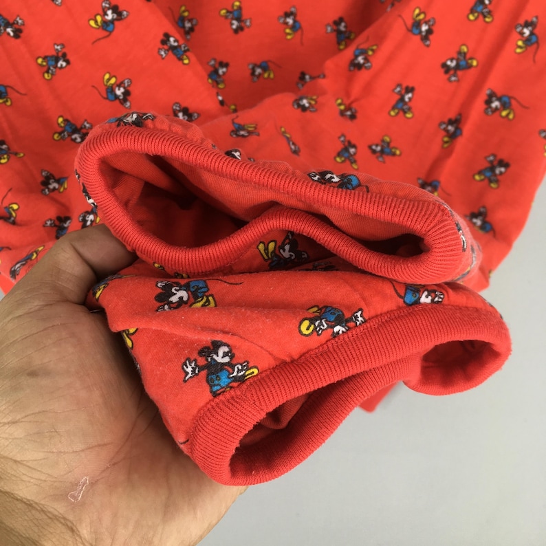 May include: Red long-sleeved shirt with a repeating pattern of Mickey Mouse in various poses. The cuffs and neckline are a solid red, and the fabric appears to be a soft knit. The shirt is likely for children or adults.