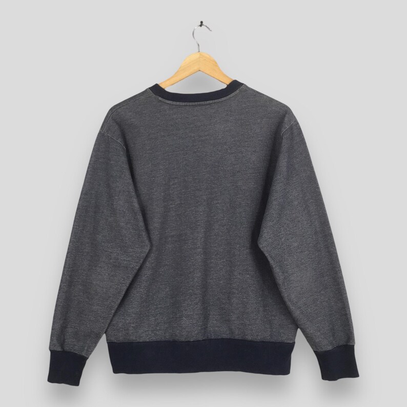 May include: A gray sweatshirt with a navy blue collar, cuffs, and hem. The sweatshirt is hanging on a wooden hanger against a plain background. The back of the sweatshirt is visible.