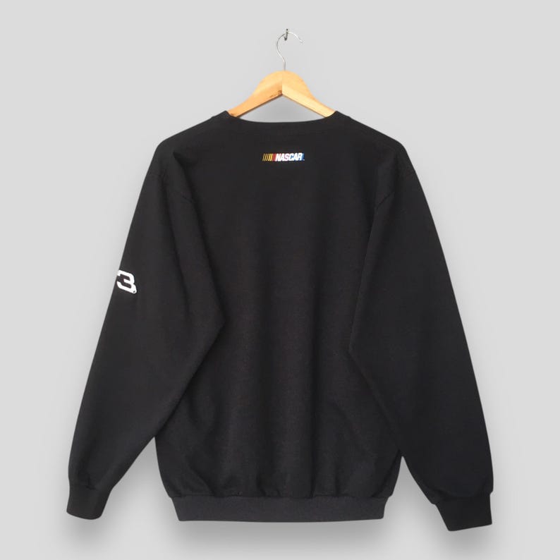 May include: Black sweatshirt with the NASCAR logo in the upper back and the number 3 on the left sleeve. The sweatshirt is hanging on a wooden hanger against a light gray background.