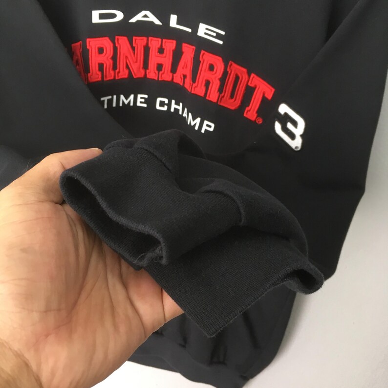 May include: Black sweatshirt with the name "DALE EARNHARDT" in red and white lettering. The number "3" is visible on the sleeve. The words "TIME CHAMP" are also displayed on the sweatshirt.