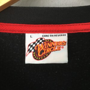 May include: Black sweatshirt with a red and black collar. The label reads "Winners Circle" with a checkered flag design. The text "Care on Reverse" is printed above the label. The size is Large.