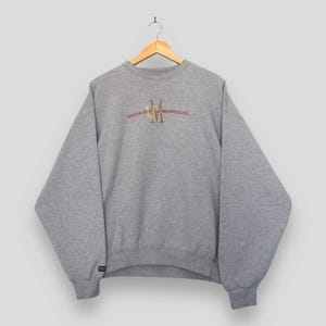 May include: A heather grey crewneck sweatshirt featuring the text University of Minnesota embroidered in red and gold across the chest. The garment has long sleeves, a ribbed collar, and a small black JanSport brand tag on the left cuff.