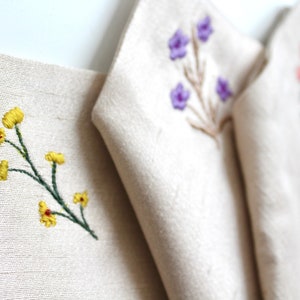 May include: Four fabric panels with different embroidered floral designs. The panels are white with yellow, purple, and pink flowers.
