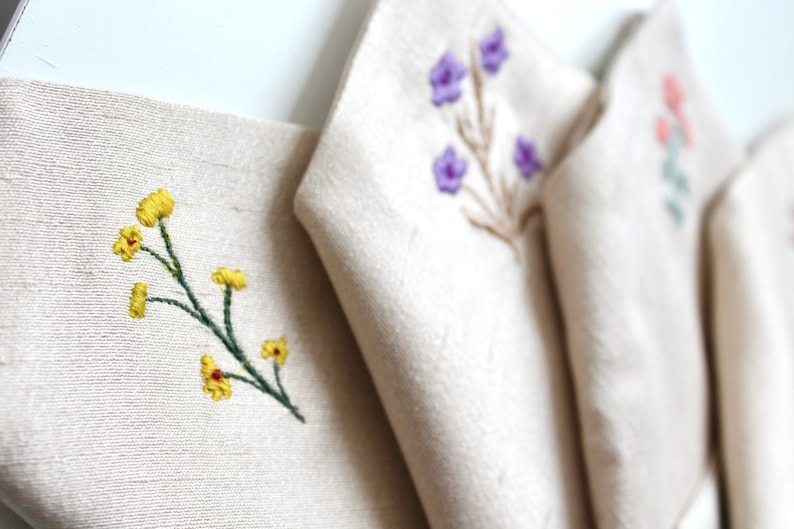 May include: Four fabric panels with different embroidered floral designs. The panels are white with yellow, purple, and pink flowers.