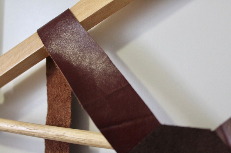 Puede incluir: Un estante de pared de madera con dos correas de cuero marr&oacute;n. El estante est&aacute; dise&ntilde;ado para sostener art&iacute;culos como sombreros, bufandas o bolsos.