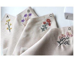 May include: Four beige linen squares with embroidered floral designs. The squares are labeled A, B, C, and D. Square A has yellow flowers, square B has purple flowers, square C has red flowers, and square D has pink flowers.