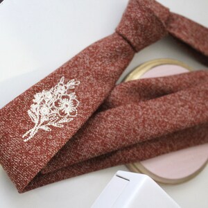May include: A brown tie with a white embroidered floral design. The tie has a textured surface.