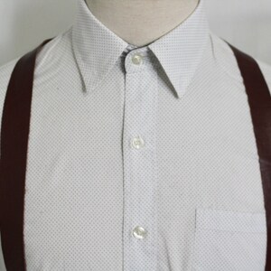 Puede incluir: Una camisa blanca de botones con un peque&ntilde;o patr&oacute;n de puntos blancos y tirantes marrones.