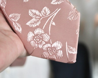 May include: A pink tie with a white floral pattern. The tie is made of a silky material and has a pointed tip.