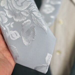 Peut inclure: Une cravate gris clair avec un motif floral blanc.