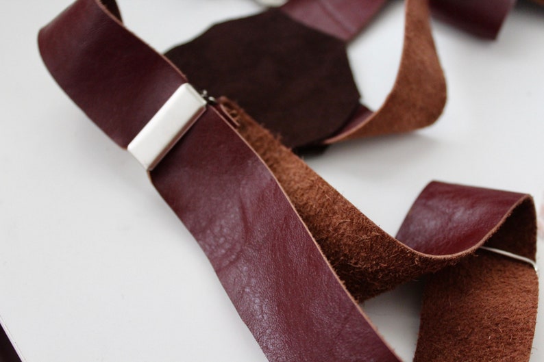 Puede incluir: Primer plano de un par de tirantes de cuero marr&oacute;n con un clip de metal plateado. Los tirantes est&aacute;n hechos de dos tipos diferentes de cuero, uno liso y otro texturizado.