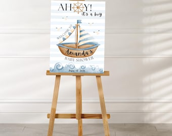 May include: A baby shower sign with a nautical theme, displayed on a wooden easel. The sign features a watercolour illustration of a sailboat, seagulls, and waves. Text includes "AH0Y! it's a boy", "Welcome to", "Amanda's BABY SHOWER", and the date June 12, 2025.