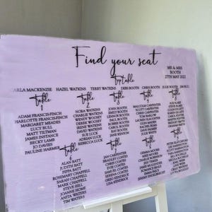 Peut inclure: Un plan de table de mariage lilas avec du texte noir. Le panneau indique "Find your seat" et répertorie les noms sous les numéros de table. La date "27 mai 2022" est également affichée.