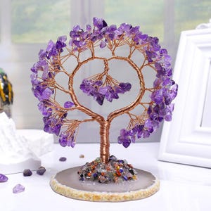 Könnte beinhalten: Eine dekorative Baumskulptur mit einem Kupferdrahtstamm und Ästen, verziert mit lila Amethyst-Edelsteinen. Der Baum steht auf einem runden, gesprenkelten Sockel. Die Edelsteine haben eine leuchtende lila Farbe.