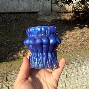 May include: A blue resin candle holder with a unique design. The candle holder has a textured surface and a glittery finish. The design features a series of rounded shapes. The holder is held in a hand.