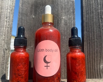May include: Three glass bottles containing red liquid with droppers. The central bottle features a pink label that reads "Lilith body oil" and includes a crescent moon and female symbol.