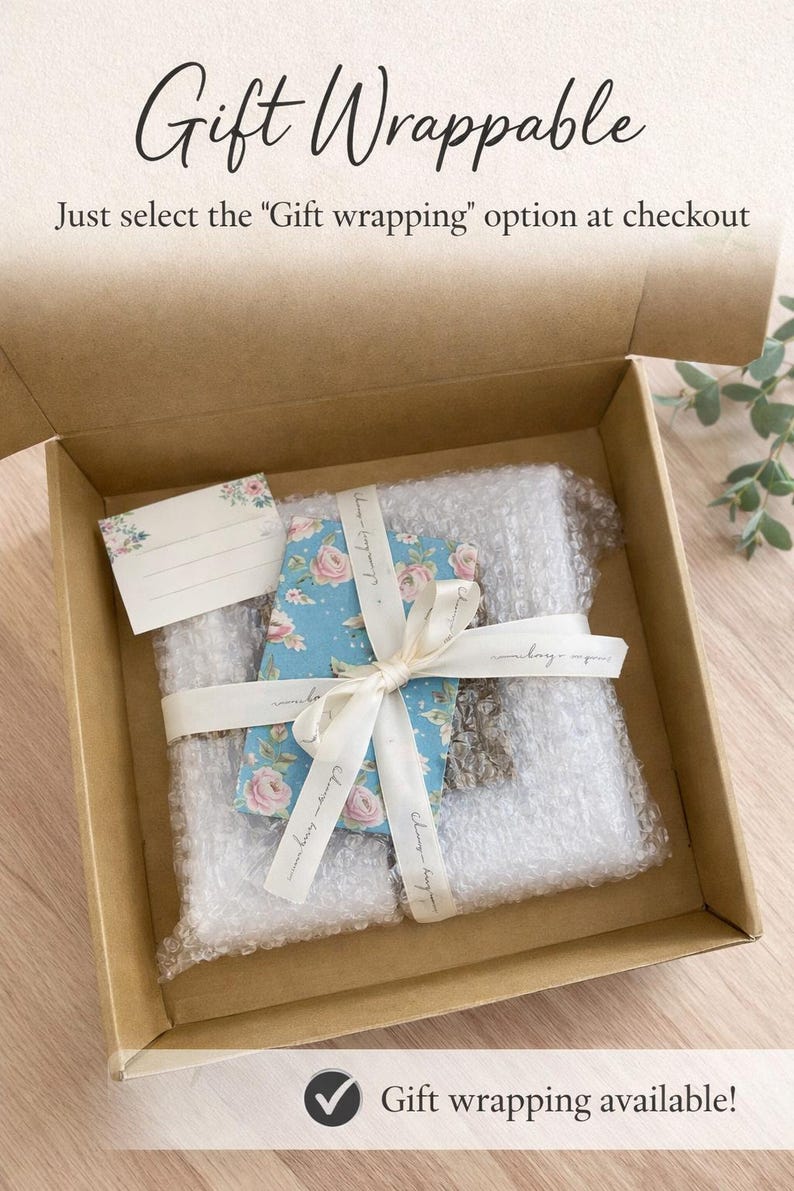 May include: A brown cardboard box containing a rectangular item wrapped in clear bubble wrap, tied with a cream-colored ribbon and a blue floral patterned card. A small blank gift tag with floral accents is included. Text reads Gift Wrappable.