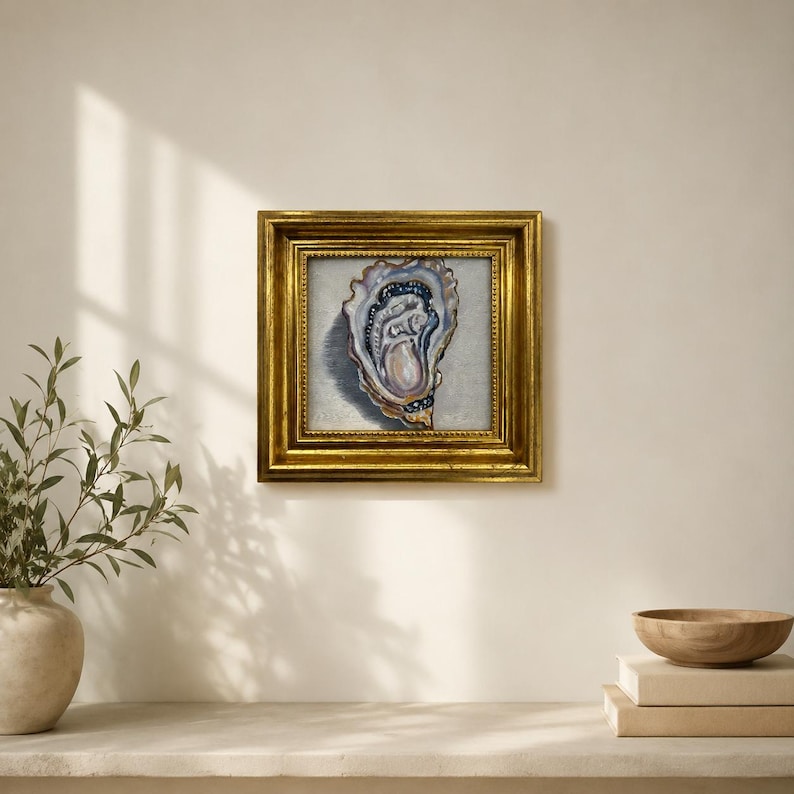 May include: A framed painting of an oyster shell. The artwork features a detailed depiction of the oyster's interior, with shades of blue, pink, and white. The painting is set within a gold-colored, ornate frame, adding a touch of elegance.