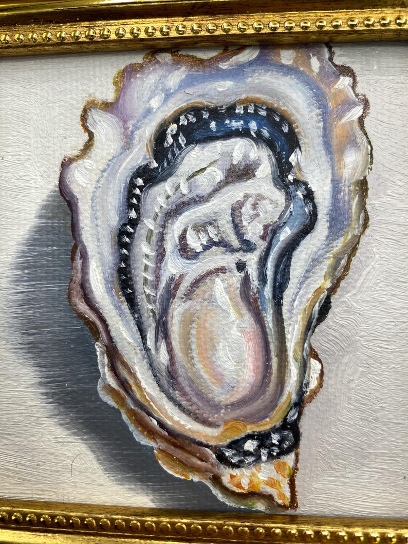 May include: Oil painting of an oyster shell in a gold frame. The shell is painted with shades of white, blue, purple, and brown. The oyster's interior has a pearlescent sheen, and the frame has a detailed, ornate design.