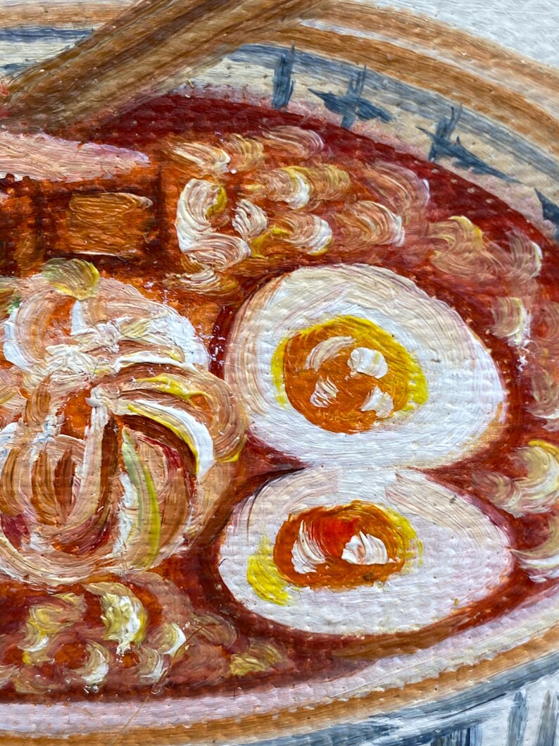 May include: An oil painting of a bowl of ramen featuring a rich red broth, two halved soft-boiled eggs with bright yellow yolks, and textured noodles. The bowl has a light-colored rim with blue decorative markings, and a wooden spoon rests inside.