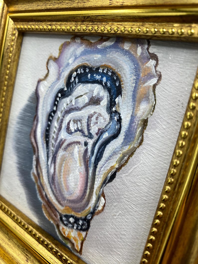 May include: Oil painting of an oyster shell in a gold frame. The shell is painted with shades of blue, white, and tan, with a dark blue interior. The frame has a beaded edge. The artwork is on a white background.