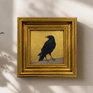May include: A square framed painting featuring a black crow perched on a ledge against a textured gold background. The ornate frame is finished in a metallic gold tone with a multi-layered, stepped profile and a beaded inner border detail.