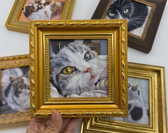 May include: A collection of framed cat portraits. The central frame features a close-up of a cat with one yellow and one blue eye. Other frames showcase different cat breeds and poses, all in ornate gold frames.