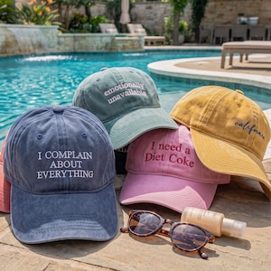 May include: A collection of five baseball caps in blue, green, pink, yellow, and coral. The blue cap reads I COMPLAIN ABOUT EVERYTHING, the green cap reads emotionally unavailable, the pink cap reads I need a Diet Coke, and the yellow cap reads california.