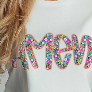 May include: White t-shirt with the word "AMEN" spelled out in colorful floral letters.
