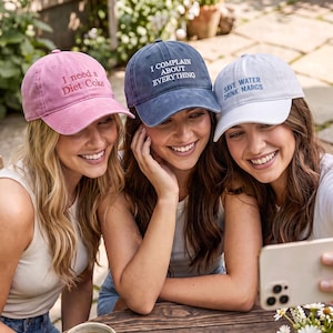 May include: Three baseball caps with embroidered text. The pink cap reads I need a Diet Coke, the blue cap reads I COMPLAIN ABOUT EVERYTHING, and the white cap reads SAVE WATER DRINK MARGS. Each cap features a curved brim and a structured crown.