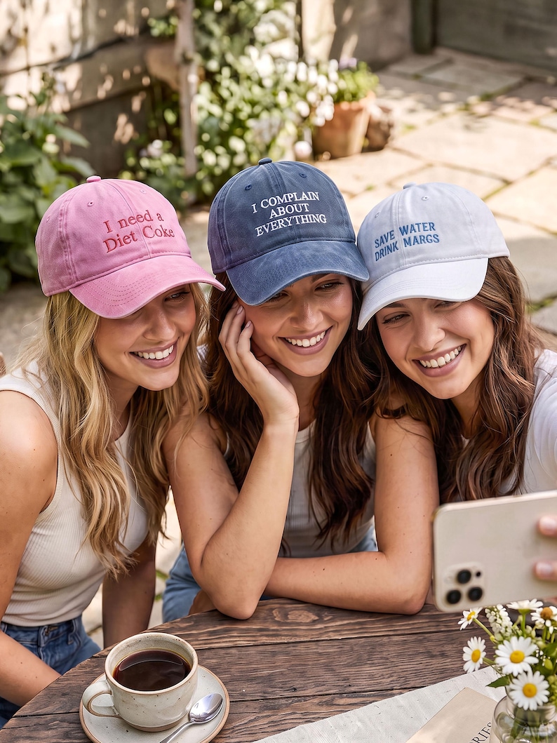 May include: Three baseball caps with embroidered text. The pink cap reads I need a Diet Coke, the blue cap reads I COMPLAIN ABOUT EVERYTHING, and the white cap reads SAVE WATER DRINK MARGS. Each cap features a curved brim and a structured crown.