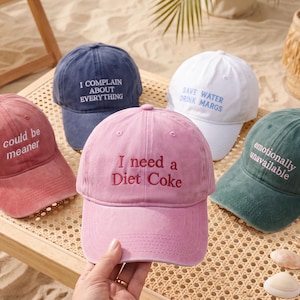 May include: Five baseball caps in various colors including pink, navy blue, white, and dark green. Each cap features embroidered text: I could be meaner, I complain about everything, Save water drink margs, I need a Diet Coke, and emotionally unavailable.
