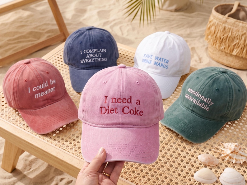 May include: Five baseball caps in various colors including pink, navy blue, white, and dark green. Each cap features embroidered text: I could be meaner, I complain about everything, Save water drink margs, I need a Diet Coke, and emotionally unavailable.