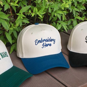 May include: Three baseball caps with embroidered text. The caps have a white crown and colored brims. One cap has "YOUR NAME" in green, another has "Embroidery Here" in blue, and the third has "Custom" in black.