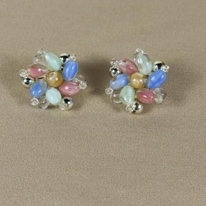 May include: A pair of cluster earrings featuring oval-shaped beads in pastel shades of pink, blue, and yellow, interspersed with small clear beads and metallic silver-toned accents arranged in a circular, flower-like pattern on each earring.