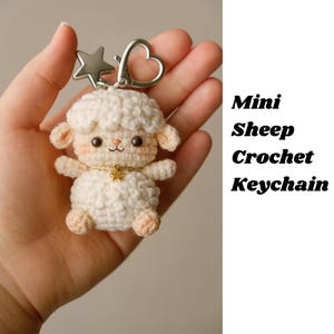 May include: A mini crochet sheep keychain with a star and heart-shaped clasp. The sheep is white with peach-colored accents on its ears, feet, and cheeks. It has a gold-colored star necklace. The text "Mini Sheep Crochet Keychain" is visible.