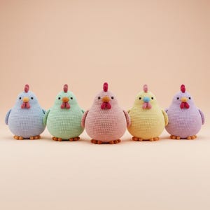 Może przedstawiać: Pięć ręcznie robionych szydełkowych kurczaków w pastelowych kolorach: jasnoniebieskim, zielonym, różowym, żółtym i fioletowym. Każdy kurczak ma czerwony grzebień, pomarańczowy dziób i małe czarne oczy. Kurczaki ustawione są w rzędzie na brzoskwiniowym tle.