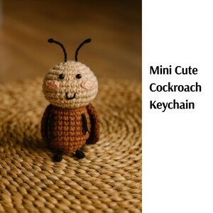 May include: A crocheted cockroach keychain. The keychain is brown with a tan head, black antennae, and small black eyes. The text "Mini Cute Cockroach Keychain" is on the right side of the image.