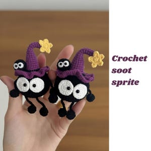 Może przedstawiać: Dwa ręcznie robione duszki sadzy na szydełku. Każdy czarny duszek ma duże białe oczy, małe czarne nogi i fioletowy kapelusz czarownicy z żółtą gwiazdą. Tekst "Crochet soot sprite" znajduje się po prawej stronie obrazu.